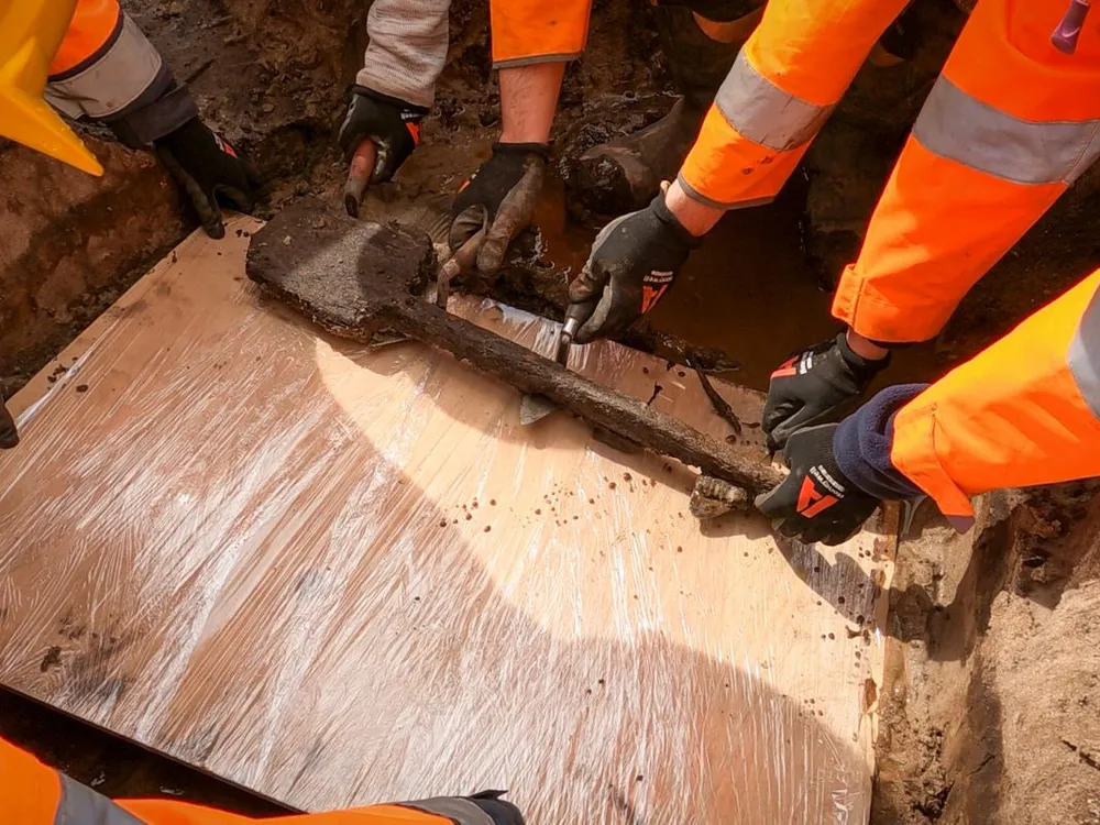 People wearing orange jackets lifting a wooden spade onto a piece of flat wood